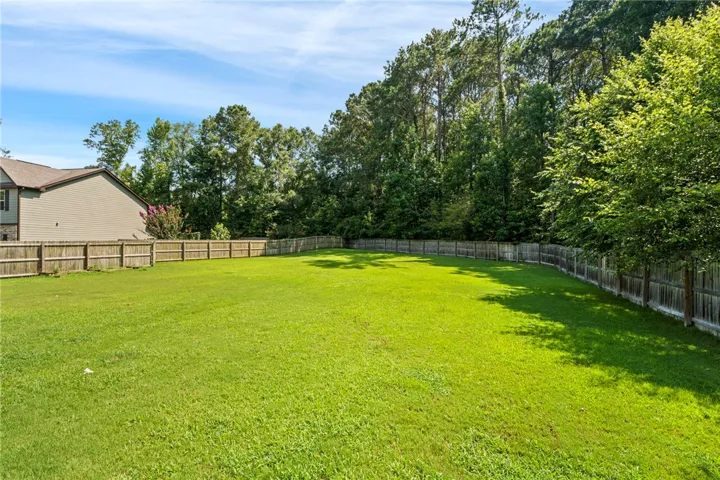 A sprawling lawn, enclosed by a privacy fence, abuts a lush, treed perimeter.