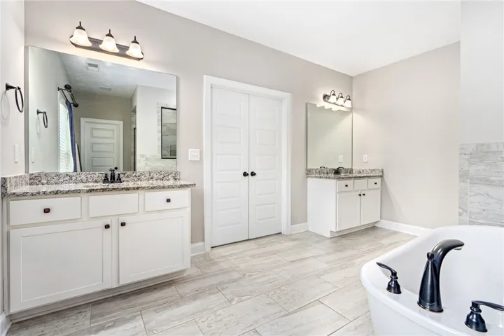 Luxurious primary bathroom featuring a freestanding tub, separate vanities, and durable tile flooring.