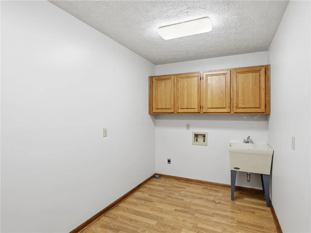 Functional laundry room featuring overhead cabinetry and a utility sink.  The laundry room is just off the kitchen and is large enough for a drop zone as well.  It is also a pass through to the garage.