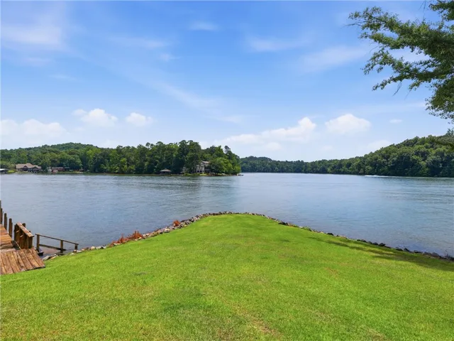 A tranquil lakefront setting, featuring a well-maintained grassy area and a private dock leading to clear waters.
