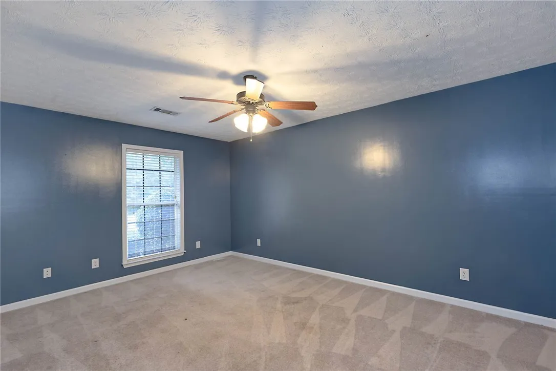 Well-lit room with ample natural light, soft carpeting, and a cooling ceiling fan.