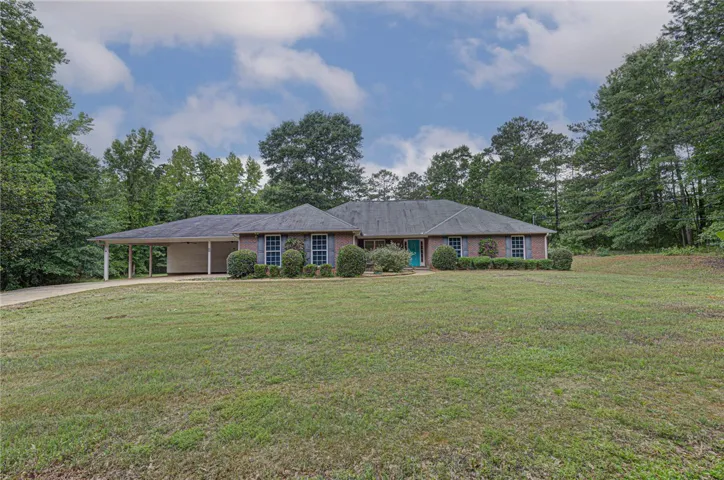 A classic brick ranch home with a spacious lawn is nestled among mature trees, offering tranquil curb appeal.