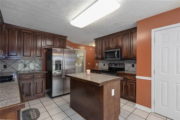 A well-appointed kitchen features rich cabinetry, granite countertops, and stainless steel appliances, all set on durable tile flooring.