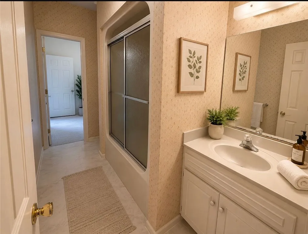 A compact bath features a combined tub and shower unit, vanity with integrated sink, and an elegant mirror.