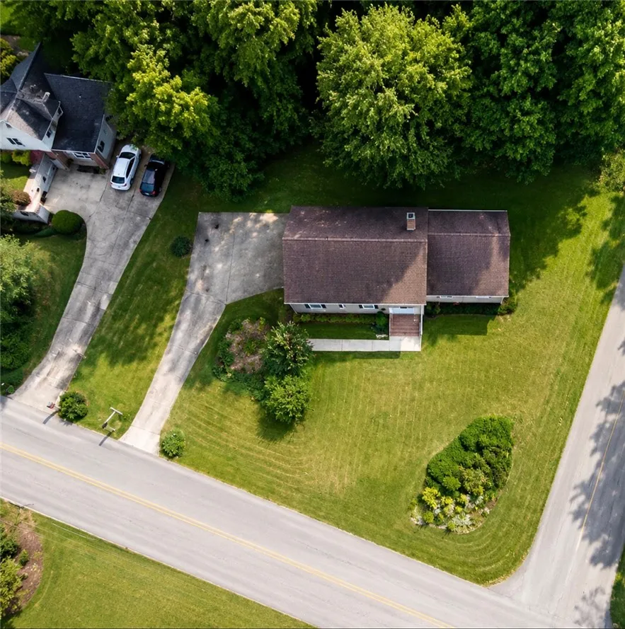 An aerial perspective showcases a home nestled amidst verdant landscaping and mature trees, featuring a concrete driveway and sidewalk.