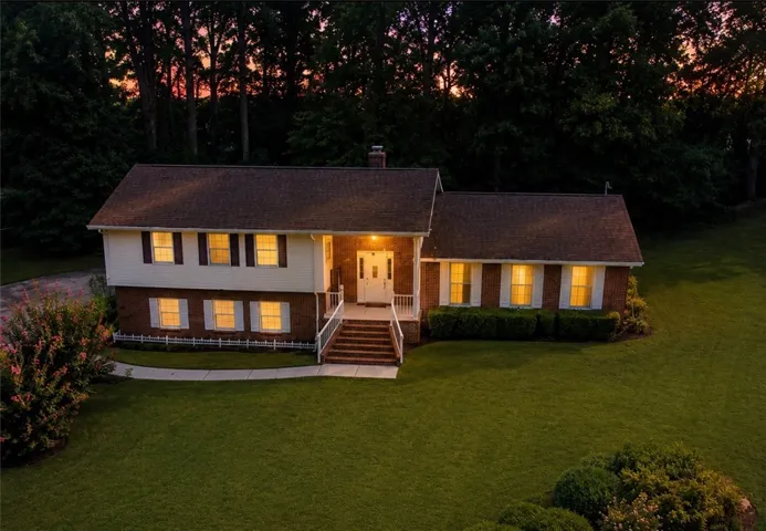 A classic brick and siding home awaits, nestled amidst a verdant landscape with mature trees.