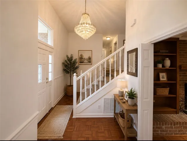 An inviting foyer features a grand chandelier, rich parquet flooring, and a classic staircase.