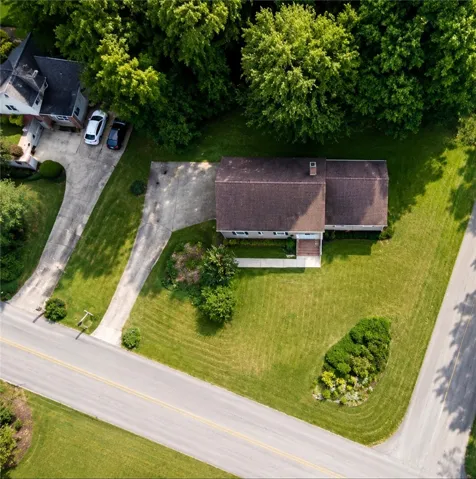 An aerial perspective showcases a home nestled amidst verdant landscaping and mature trees, featuring a concrete driveway and sidewalk.
