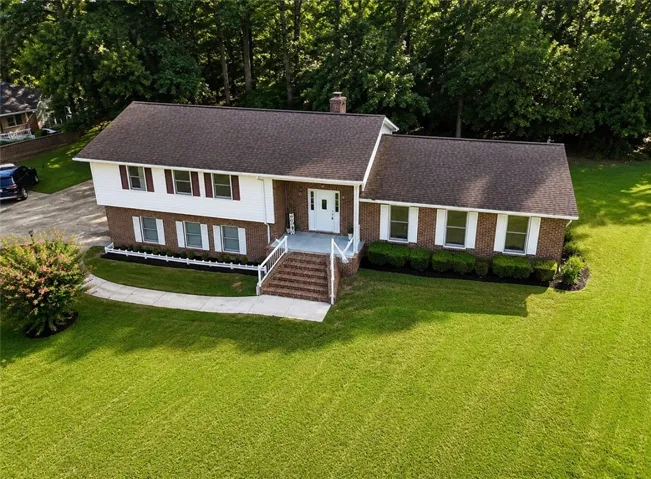 A classic brick-front home with white siding and lush green landscaping awaits.