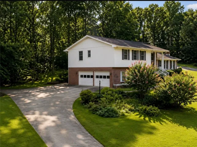 A split-level residence with a lower-level garage is nestled among mature trees and lush landscaping.
