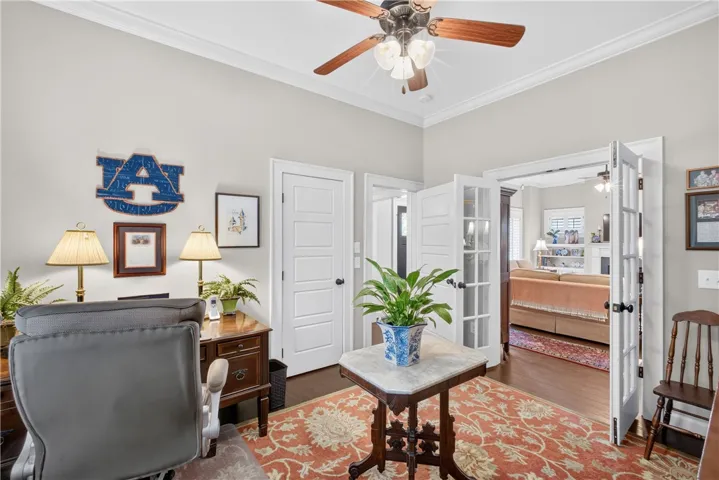 French doors open into this refined study, featuring rich hardwood flooring and a classic ceiling fan.