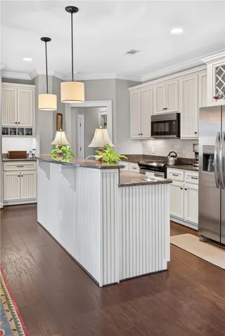 Well-lit kitchen with dark hardwood floors, beadboard cabinetry, and stainless steel appliances.