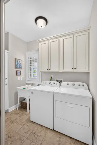 Functional laundry room equipped with upper cabinetry, a utility sink, and ample space for appliances.