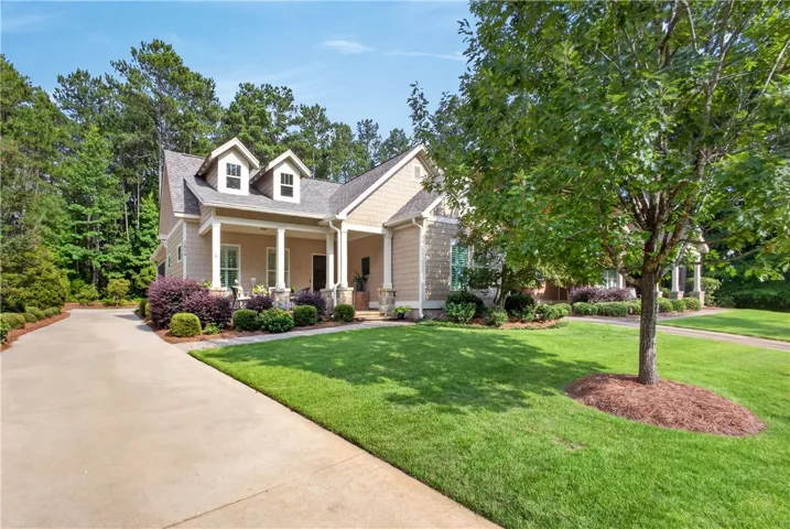 A graceful home with a welcoming front porch is set against a backdrop of lush trees and a manicured lawn.