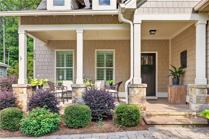 A welcoming stone and wood-shingled facade, framed by lush landscaping and a cozy covered porch, provides exceptional curb appeal.