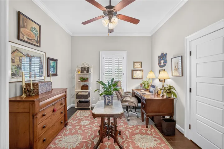 A well-lit study with wood flooring features crown molding and a decorative area rug.
