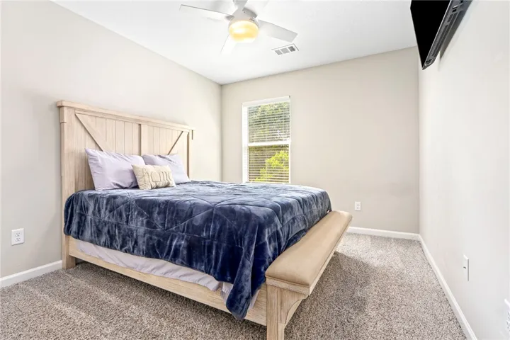 A naturally illuminated bedroom offers comfort with soft carpeting and a ceiling fan for climate control.