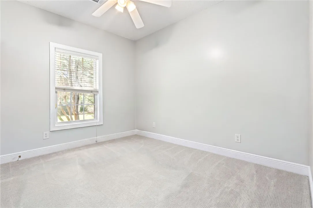 A well-lit bedroom features plush carpeting and a bright window overlooking the natural surroundings.