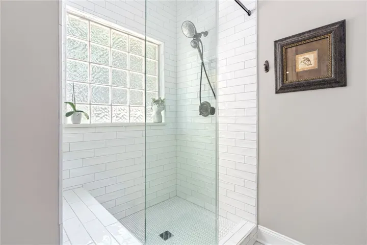 A glass-enclosed shower boasts a tiled bench and a window providing privacy and natural illumination.