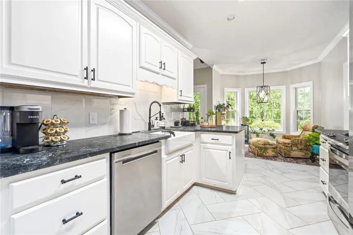 A pristine kitchen features soapstone countertops, white cabinetry, and a bright, well-lit breakfast area.