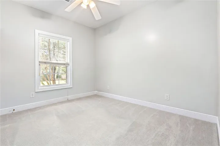 A well-lit bedroom features plush carpeting and a bright window overlooking the natural surroundings.