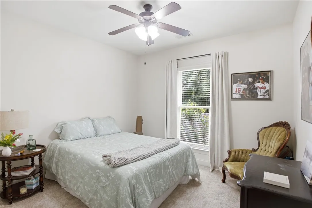 A well-lit bedroom features plush carpeting and a ceiling fan for comfort.