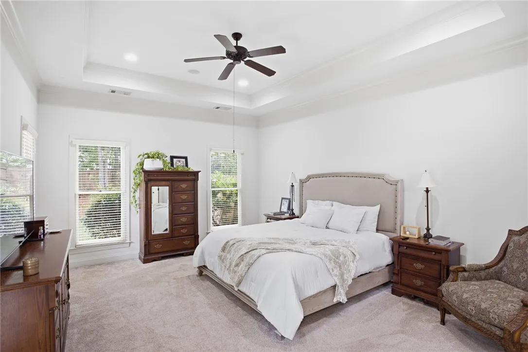 A well-lit bedroom features a tray ceiling and lush carpeting, offering a peaceful retreat.