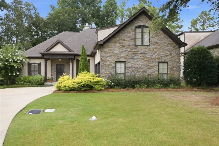 A stone and stucco facade adorns this charming residence, framed by mature trees and manicured landscaping.