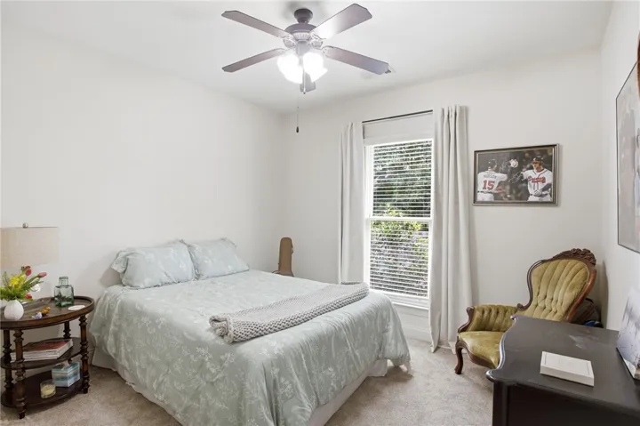 A well-lit bedroom features plush carpeting and a ceiling fan for comfort.