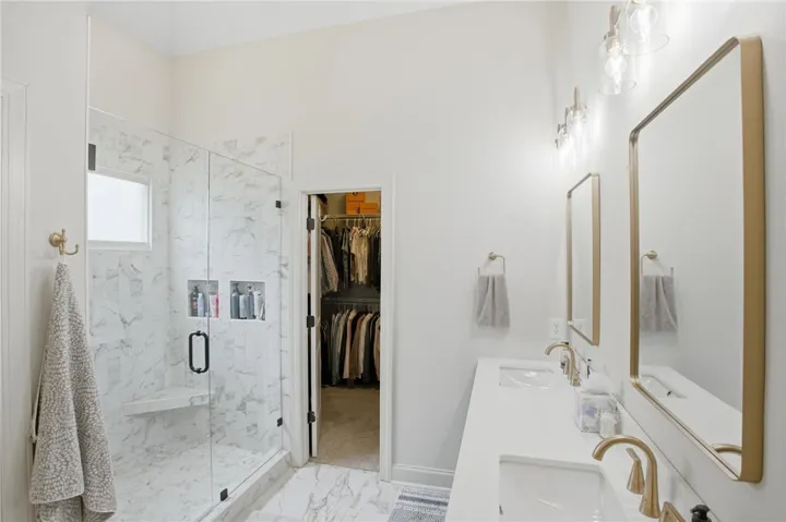Marble-tiled shower with glass enclosure leads to a spacious walk-in closet in this elegant primary bathroom.