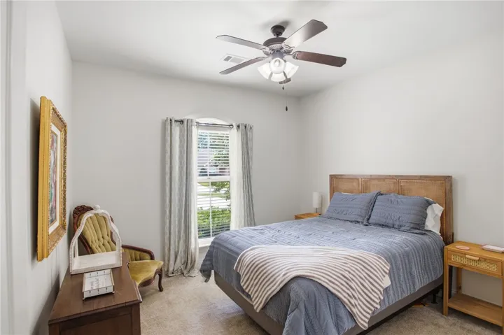 A well-lit bedroom offers comfortable living with a prominent window and ceiling fan.