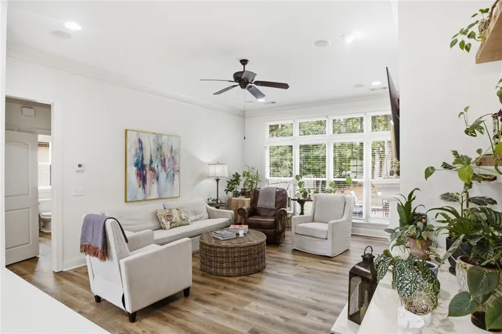 A naturally illuminated living room features durable wood flooring, high ceilings, and a large window overlooking lush greenery.