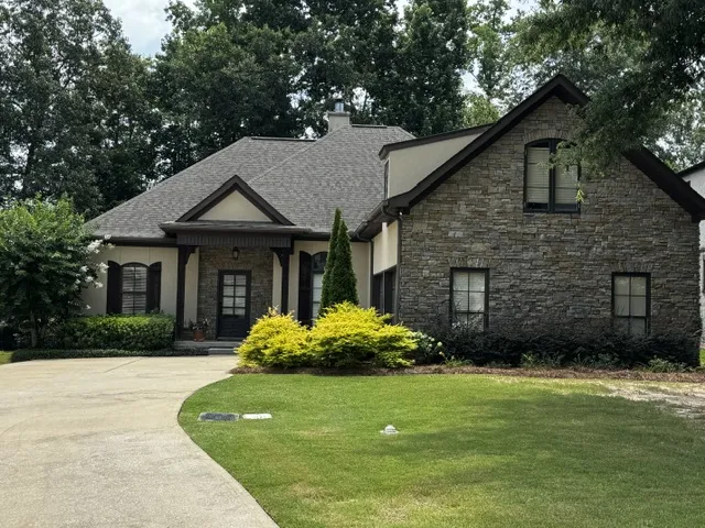 An inviting stone and stucco facade greets guests along a gracefully curved driveway.
