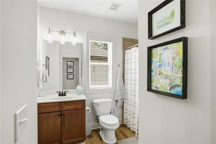 A full bathroom featuring warm wood-look flooring and a functional vanity with a sleek faucet.