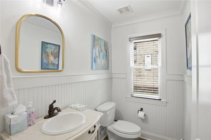 A pristine powder room offers wainscoting and natural light from a window with privacy blinds.