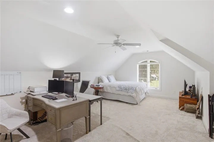 A spacious, naturally illuminated room featuring an arched window, plush carpeting, and a practical workspace.