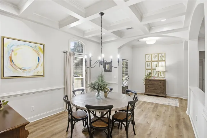 Elegant coffered ceilings crown this refined dining space, showcasing rich hardwood flooring and a stylish chandelier.