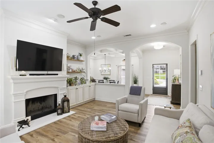A well-lit living space, featuring a classic fireplace and broad plank flooring, opens gracefully into an inviting dining area.