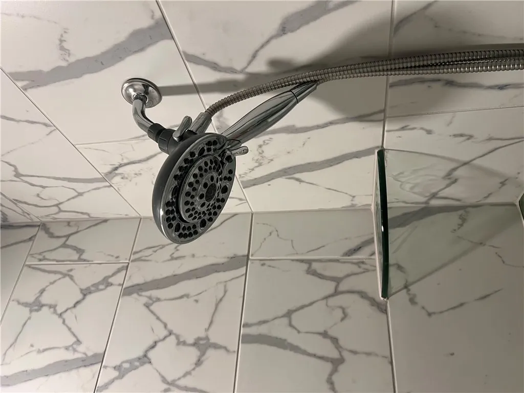 Marbled tile lines the shower, featuring a multi-setting showerhead. Goes all the way to the ceiling