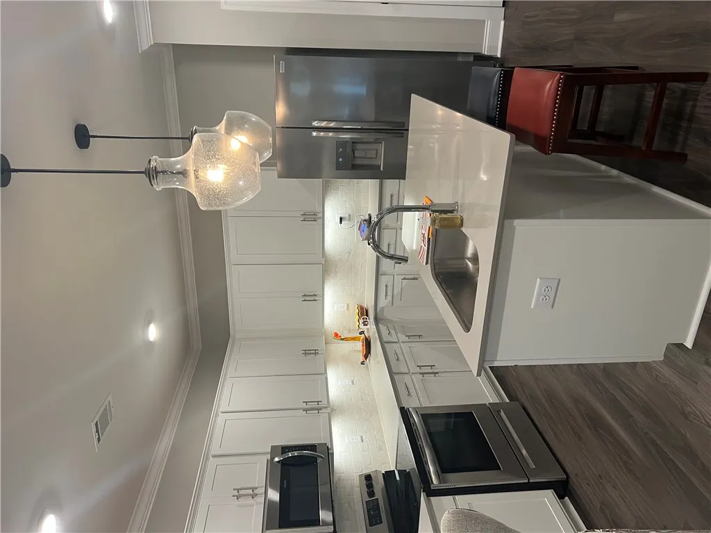 A contemporary kitchen features bright white cabinetry, stainless steel appliances, and a central island with a sink.