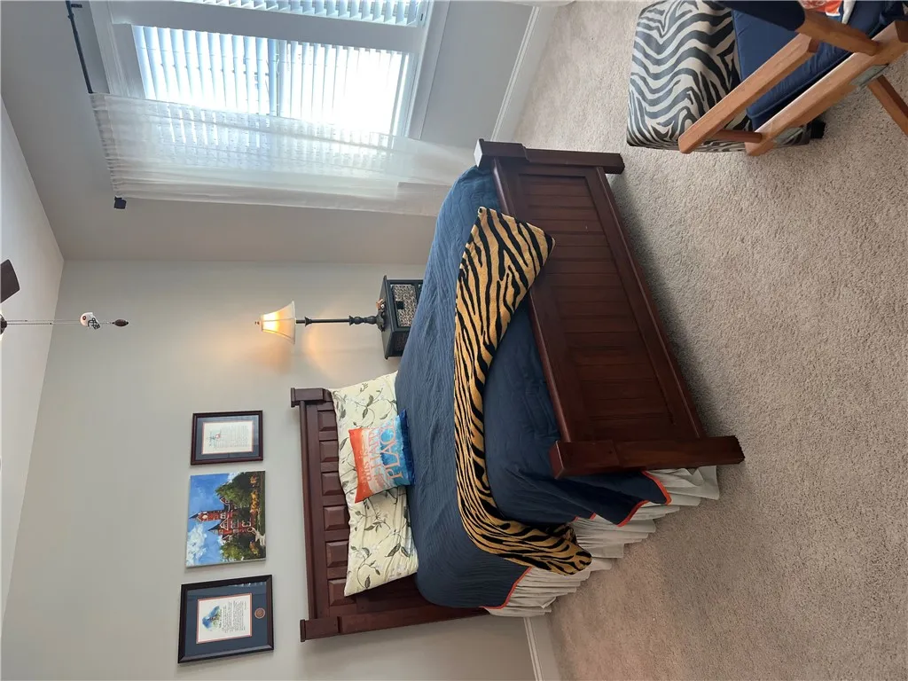 A well-lit 2nd bedroom sleeping area features a rich wooden bed frame and plush carpeting, creating a tranquil retreat.