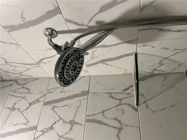 Marbled tile lines the shower, featuring a multi-setting showerhead. Goes all the way to the ceiling