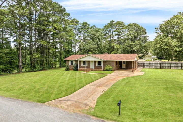 A classic brick ranch home nestled among mature trees with an inviting front yard and concrete driveway.