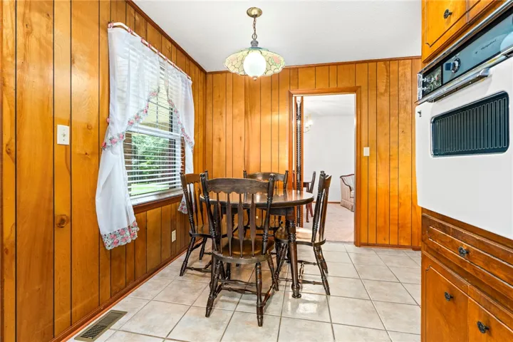 A cozy dining area features a classic wooden table set against warm paneled walls, with a charming window offering natural light.