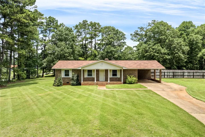 A classic brick ranch home nestled among mature trees with an inviting front porch and a wide-open lawn.