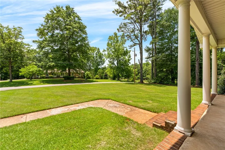 A classic covered porch with stately columns overlooks a verdant, well-maintained lawn and mature trees.