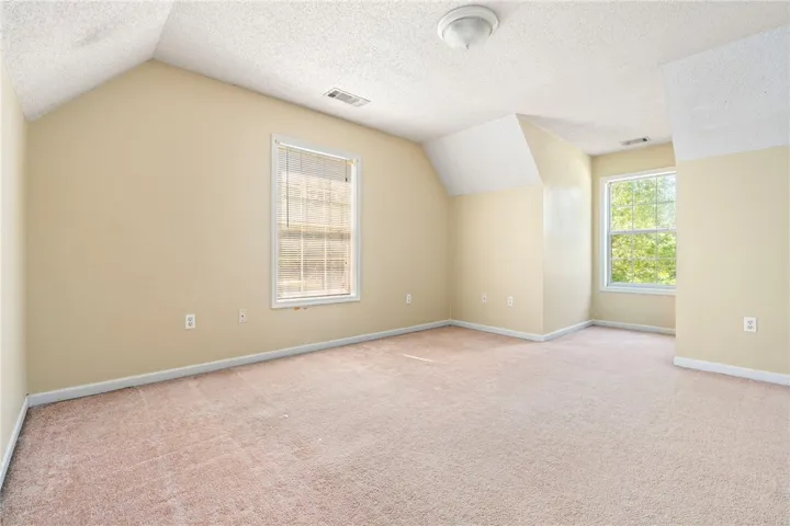A spacious room offers comfortable carpet flooring and abundant natural light from multiple windows.