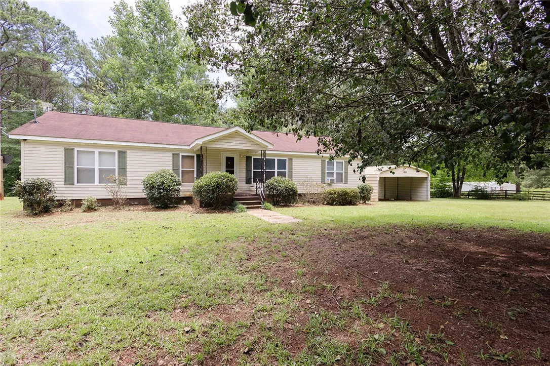A welcoming residence featuring a covered front entry and a convenient carport, set amidst a verdant landscape.