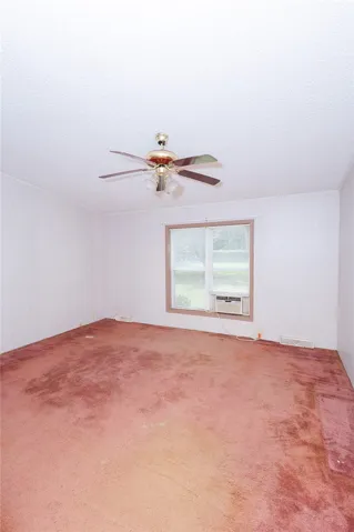 A window unit provides cooling in this bedroom, complete with a ceiling fan and wall-to-wall carpeting.
