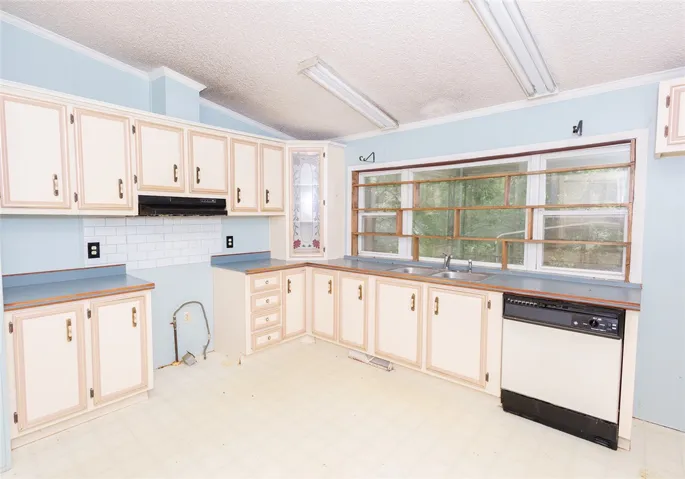 A functional kitchen with light blue walls, featuring ample cabinetry and a window overlooking a verdant outdoor space.